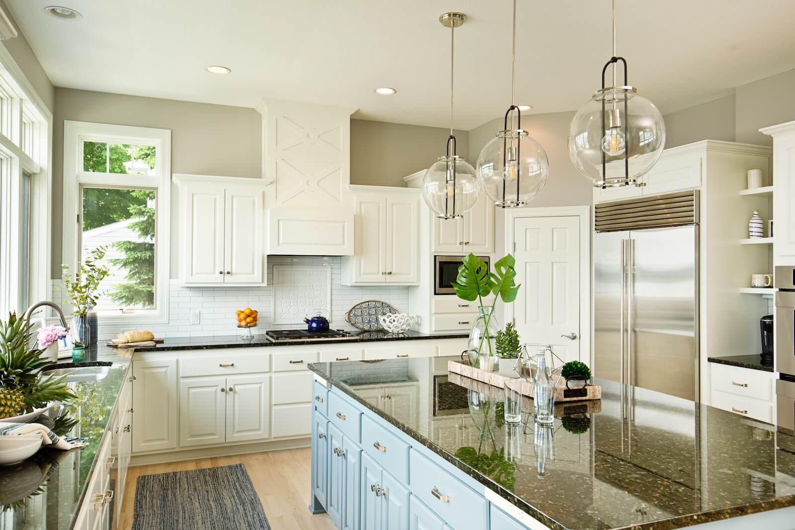 Bright kitchen with white cabinets and blue island under glass pendant lights.