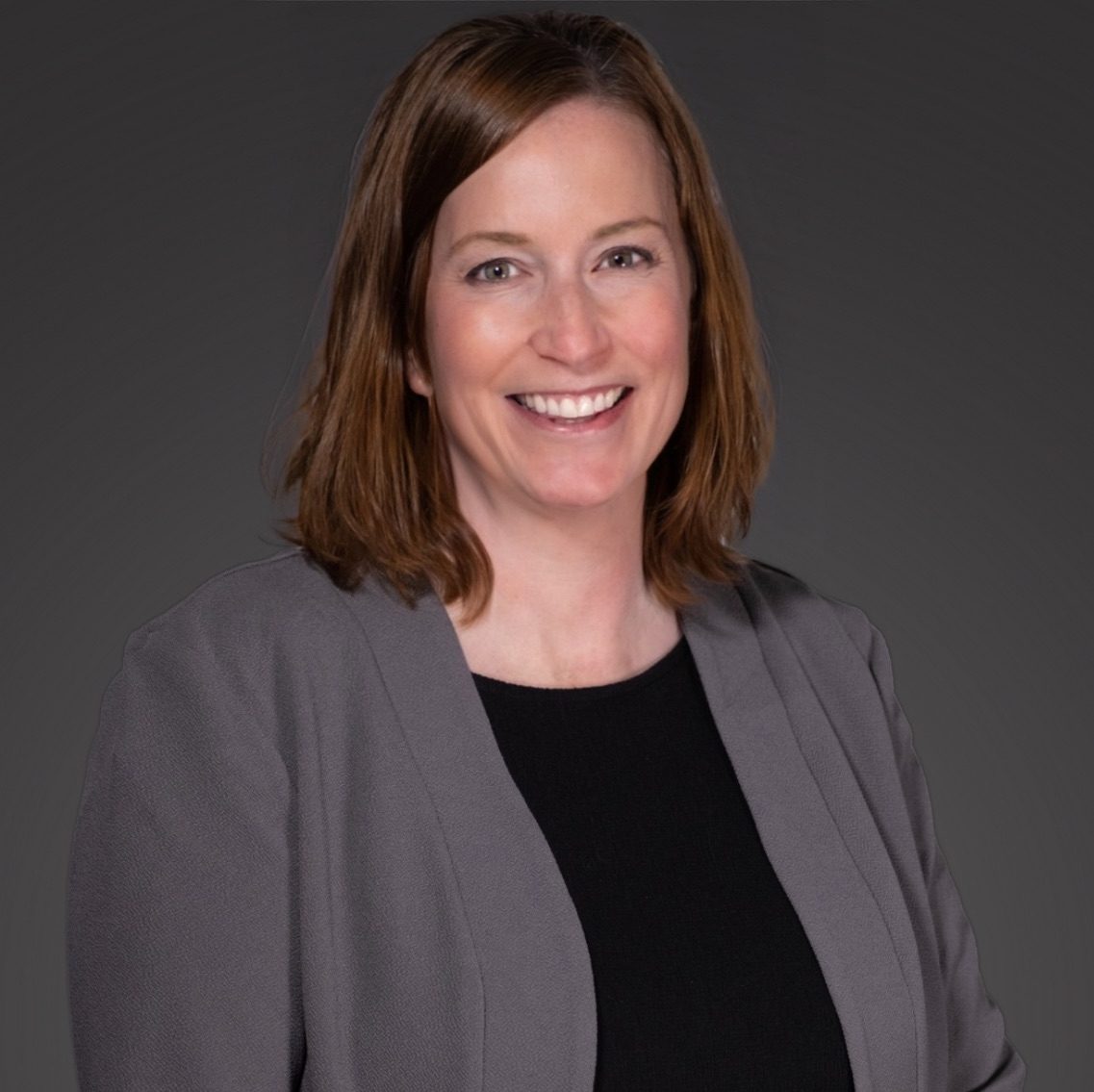 Professional woman smiling in a grey blazer and black top.