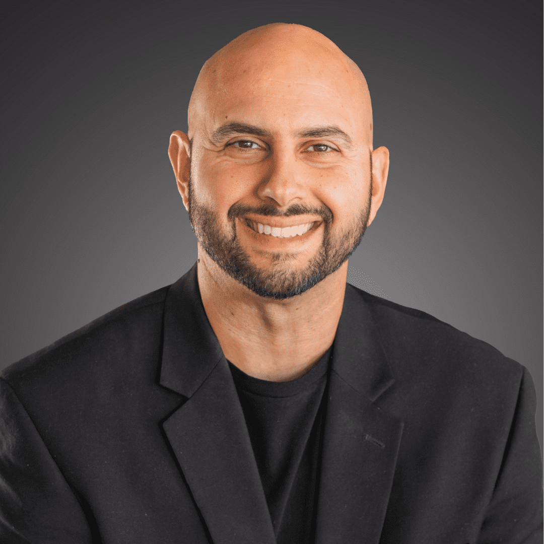 Smiling bald man in a black blazer against a gray background.