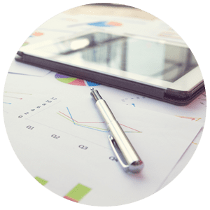 Pen resting on business charts with a tablet in the background.