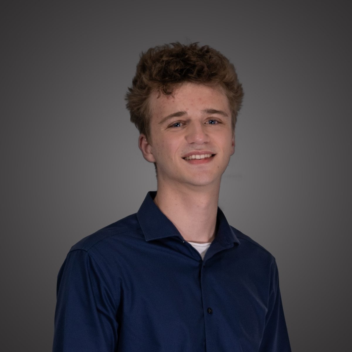 Young man with curly hair smiling in a studio portrait.